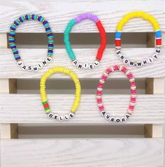 four colorful bracelets with words written on them in different colors and sizes, arranged against a white wooden background