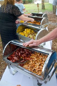 people are serving themselves food from trays on a buffet table in a park setting