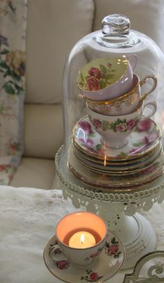 a glass clochet with cups and saucers under it next to a lit candle