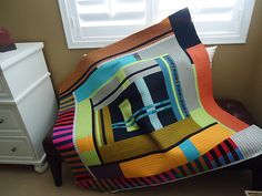 a multicolored blanket sitting on top of a bed next to a white dresser