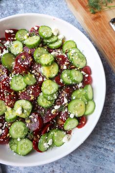 a white bowl filled with cucumbers covered in feta cheese and red sauce