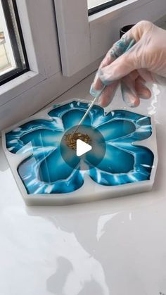 a person in white gloves is painting a flower on a glass plate with blue paint