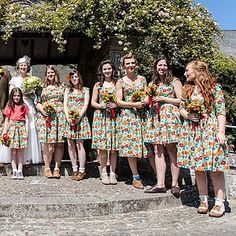 a group of women standing next to each other in front of a stone building with flowers on it