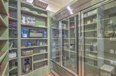 an empty glass doored refrigerator in a room with shelves full of food and condiments