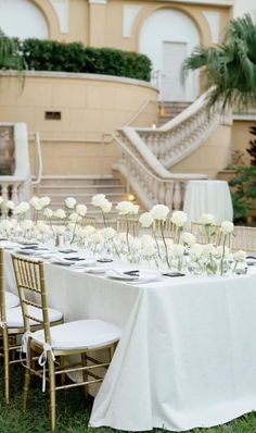 a long table with white flowers on it in front of a building and stairs leading up to the second floor