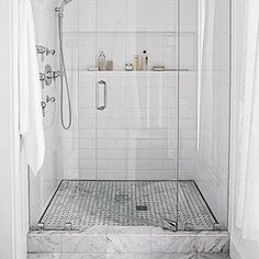 a walk in shower sitting next to a white tiled wall and floor covered in towels