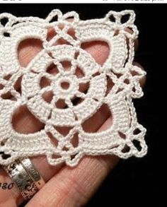 a white crochet doily is held in someone's hand with a ring on it