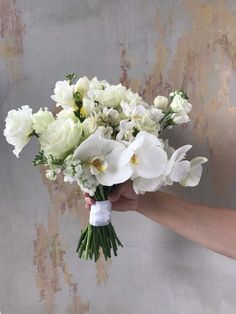 a person holding a bouquet of white flowers in their left hand, against a grungy wall