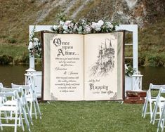 an open book sitting on top of a grass covered field next to white chairs and flowers