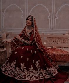 a woman in a red and gold wedding dress sitting on a bench