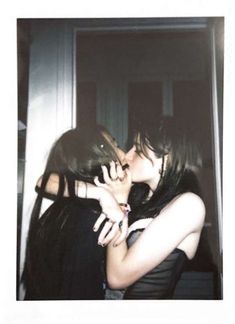 two young women kissing each other in front of a door with their arms around one another