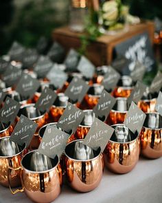 there are many copper cups with name tags on them sitting on a white table cloth