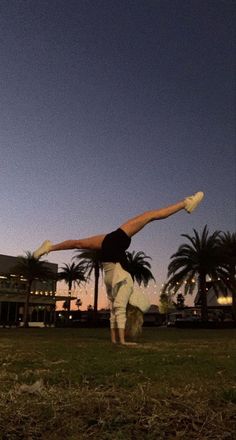 a person is doing a handstand on the grass in front of palm trees