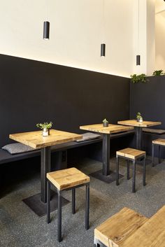 an empty restaurant with wooden benches and plants on the tables in front of black walls