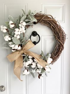 a wreath with cotton and greenery hanging on the front door, next to an iron hook