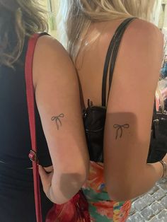 two women with matching tattoos on their arms and backs, both wearing black bras