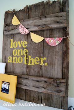 a wooden sign that says love one another with bunting on it and some pictures