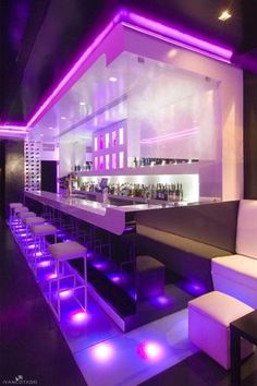 the bar is lit up with purple lights and white stools in front of it