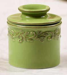 a green canister with an ornate design on the top and bottom, sitting against a white background