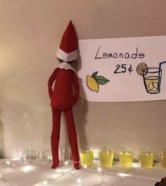 an elf standing next to a sign with lemonade on it and glasses in front of him