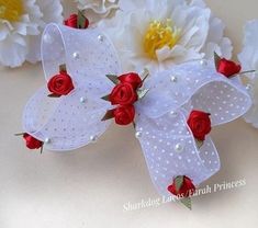 two red roses and white mesh angel wings with pearls on each side, surrounded by flowers