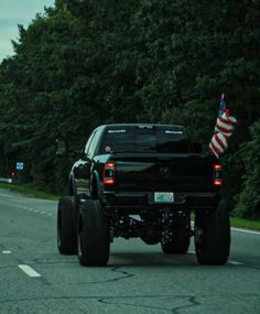 a black truck driving down the road with an american flag on it's tail