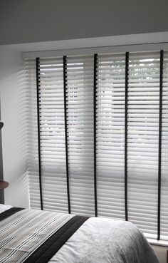 a bed sitting next to two windows with blinds on it's sides, in front of a white wall