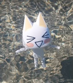 a paper cat floating in the water with its eyes closed and tongue out, looking like it's smiling