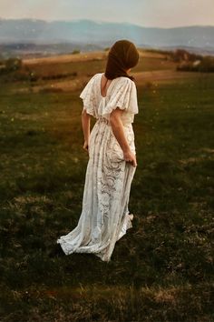 a woman in a white dress is standing on the grass with her back to the camera