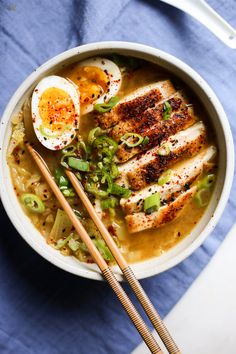 a bowl filled with chicken and vegetables next to chopsticks on a blue table cloth