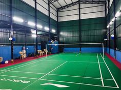 an indoor tennis court with two people playing on the sidelines and chairs around it