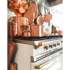 copper pots and pans are hanging on the wall above an oven in a kitchen