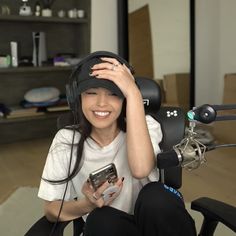 a woman sitting in a chair holding a cell phone and wearing a hat with her hands on her head