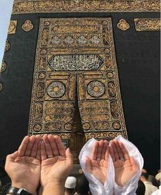 two hands are raised up to pray in front of the kabab, which is decorated with gold and black