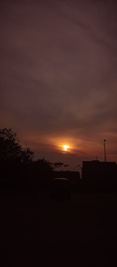 the sun is setting over some buildings and trees in front of a dark cloudy sky