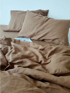 an unmade bed with brown sheets and pillows