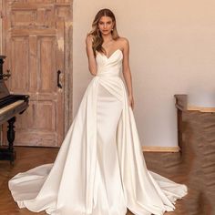 a woman standing in front of a piano wearing a wedding dress with an asymmetrical neckline