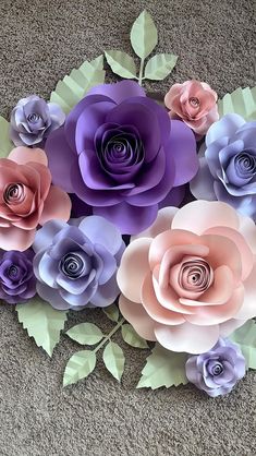 paper flowers arranged on the ground with leaves and stems in purples, pinks and lavenders