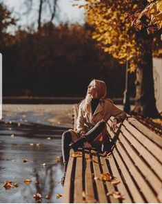 a woman sitting on top of a wooden bench next to a tree filled with leaves