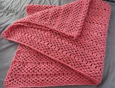 a pink crocheted blanket laying on top of a bed next to a pillow