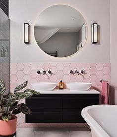 a bathroom with two sinks and a large round mirror above the double sink, next to a bathtub