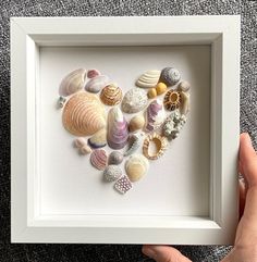 a heart made out of seashells is displayed in a white frame on the carpet