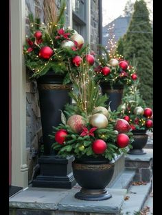 christmas decorations are lined up on the front steps in black urns with red and gold ornaments