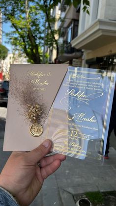 a person holding up two wedding cards in front of a building on a street corner