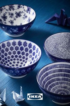 three blue and white bowls with origami cranes in the background on a table