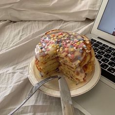 a laptop computer sitting on top of a bed next to a stack of pancakes covered in sprinkles