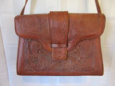 "Great vintage bag from the 60s or 70s, Mexican style, by Deer Products. Tooled leather. Floral designs. Suede interior. Marked Deer Products on the bottom with a deer image. 11 inches across at the widest point, bottom edge. 7-3/4 inches high. 2 adjustable straps adds another 10-1/2 inches to 15 inches. 4-3/4 inches deep at the widest, bottom. Open large pocket along the exterior back. Clean interior is divided into 2 sections, with a zippered pocket section in the middle. 4 flat metal \"feet\" Vintage Brown Hand Tooled Satchel, Vintage Brown Hand-tooled Satchel, Mid-century Brown Shoulder Bag For Travel, Brown Travel Bags, Vintage Saddle Bag In Vintage Brown, Retro Brown Hand Tooled Shoulder Bag, Brown Retro Shoulder Bag With Hand Tooled Details, Retro Brown Hand-tooled Satchel, Vintage Brown Saddle Satchel