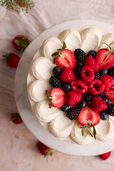 a white cake topped with strawberries and blueberries on top of a white plate