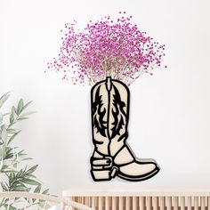 a vase filled with purple flowers next to a wall mounted cowgirl boot on top of a wooden table