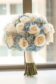 a bouquet of white roses and blue hydrangeas sits on a window sill